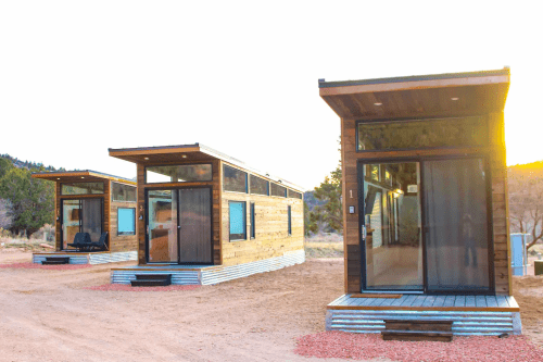 Three modern tiny houses with large windows, set in a natural landscape during sunset.